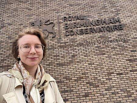 Birmingham: Clara Schina vor dem Logo des Royal Birmingham Conservatoire/Foto: Clara Schina Das Logo des Royal Birmingham Conservatoire auf einer Mauer
