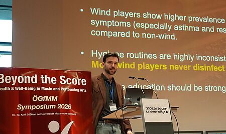 Dr. Breaden Madden präsentiert die Ergebnisse der Studie auf dem Symposium der Österreichischen Gesellschaft für Musik und Medizin (ÖGfMM) in Salzburg/Foto: MDW Dr. Breaden Madden hält einen Vortrag vor einer digitalen Präsentation