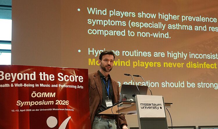 Dr. Breaden Madden präsentiert die Ergebnisse der Studie auf dem Symposium der Österreichischen Gesellschaft für Musik und Medizin (ÖGfMM) in Salzburg/Foto: MDW Dr. Breaden Madden hält einen Vortrag vor einer digitalen Präsentation, to the current article