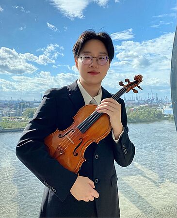 Langyu Qin mit Violine, im Hintergrund Wasser und eine Stadt
