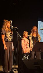 Projekt Musik macht Welt/Foto: Esther Kaiser Zwei STudentinnen stehen mit Schülerin auf der Bühne