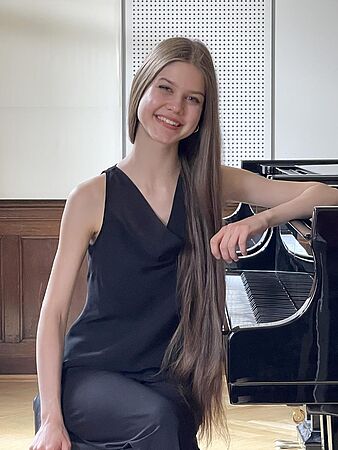 Stefaniia Zubko lehnt sich auf das Klavier und lächelt