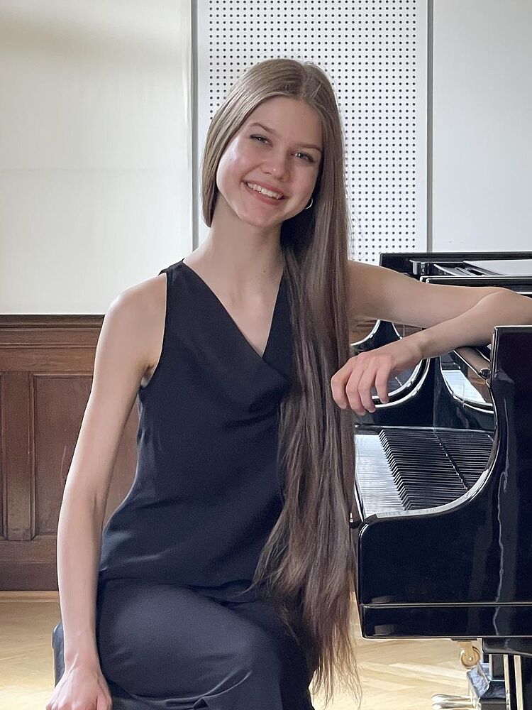 Stefaniia Zubko lehnt sich auf das Klavier und lächelt, zum Aktuelles-Beitrag