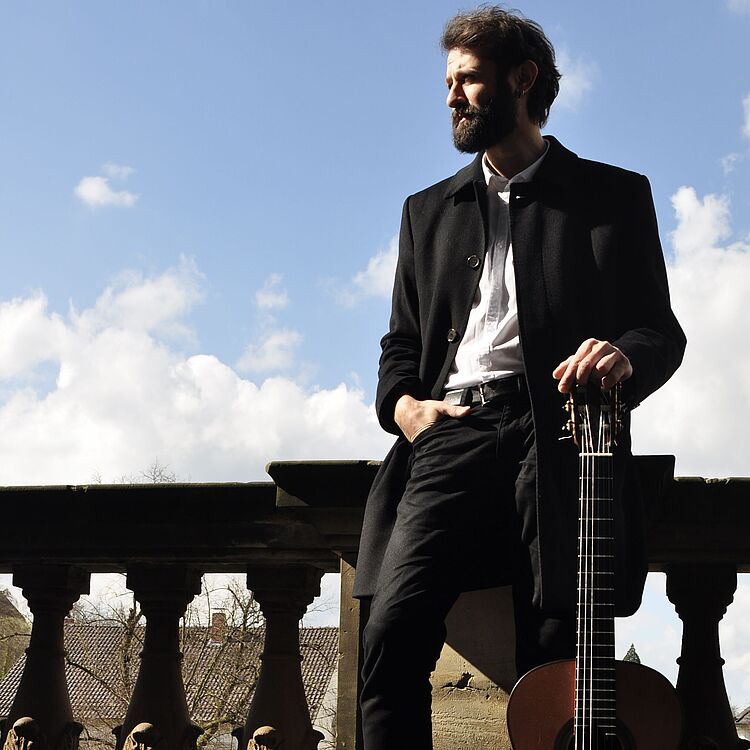 Ozan Coskun mit Gitarre auf einer Balustrade, to the current article