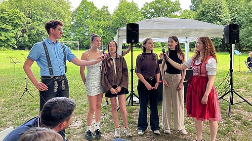 Schüler*innen stehen nebeneinander, bekommen ein Mikrofon gehalten und singen