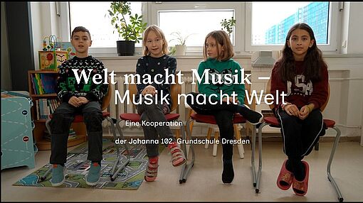 Vier Kinder sitzen nebeneinander auf Stühlen vor einem Fenster