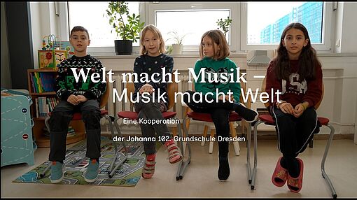 Vier Kinder sitzen nebeneinander auf Stühlen vor einem Fenster