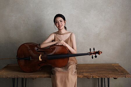 Jinxuan Hu sitzt mit ihrem Cello auf einer Bank
