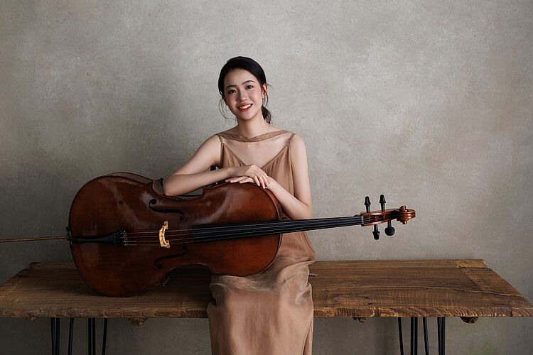 Jinxuan Hu sitzt mit ihrem Cello auf einer Bank, zum Aktuelles-Beitrag